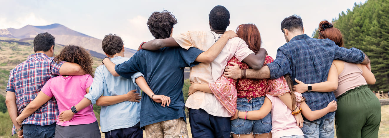 Grupo de personas abrazadas y unidas, de espaldas, mirando al horizonte en un entorno natural.