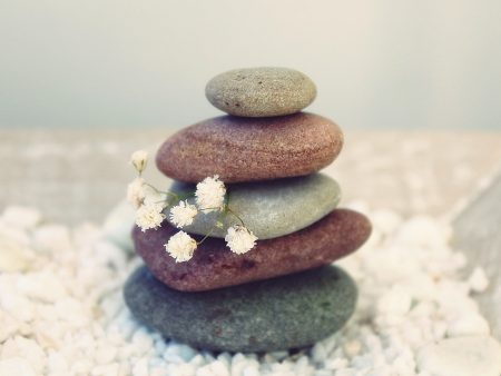 Piedras de colores apiladas sobre un lecho de flores blancas, representando el equilibrio y la calma.