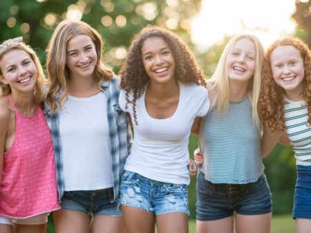 Grupo de chicas adolescentes sonriendo y abrazándose al aire libre, mostrando felicidad y amistad.